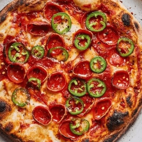 A close-up of a Li'l Nick's Pizza with pepperoni, jalapeños, and a crispy crust.