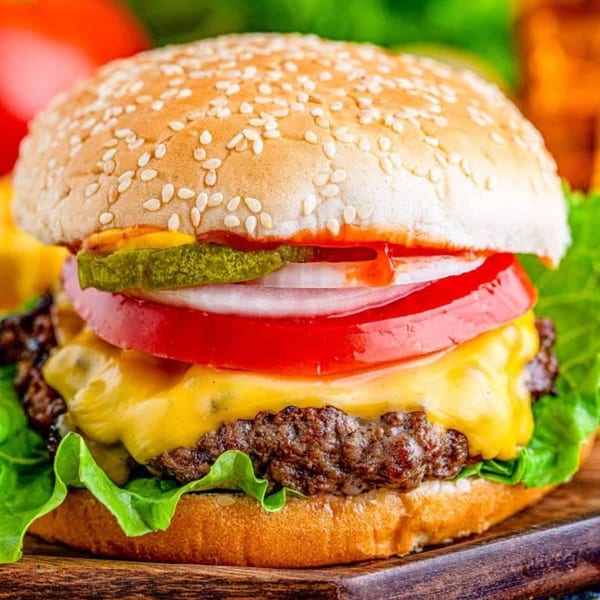 Cheeseburger with melted cheese, lettuce, tomato, onion, pickles, and ketchup on a sesame seed bun.
