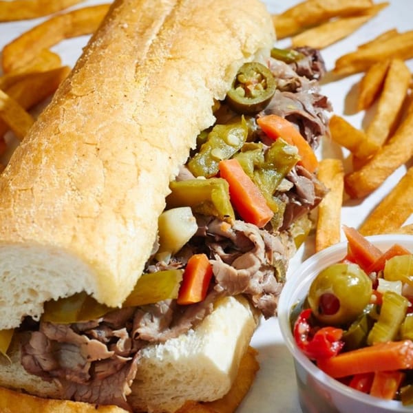 A Li'l Nick's Italian beef sandwich with giardiniera, fries, and a side of pickled vegetables.