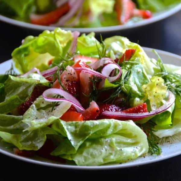 Fresh green salad with red onions, strawberries, and dill, seasoned with pepper.