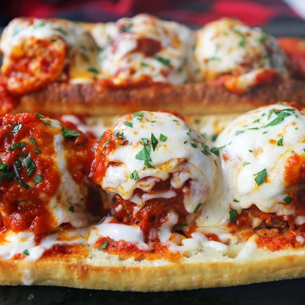 Close-up of a Li'l Nick's Pizza meatball sub, topped with melted mozzarella, marinara, and parsley.